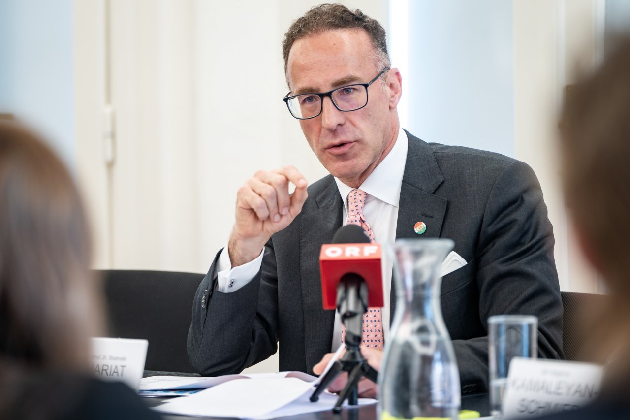 Ein Mann spricht sitzend im Rahmen einer Pressekonferenz. Vor ihm ist ein Mikrophon eines TV-Senders.