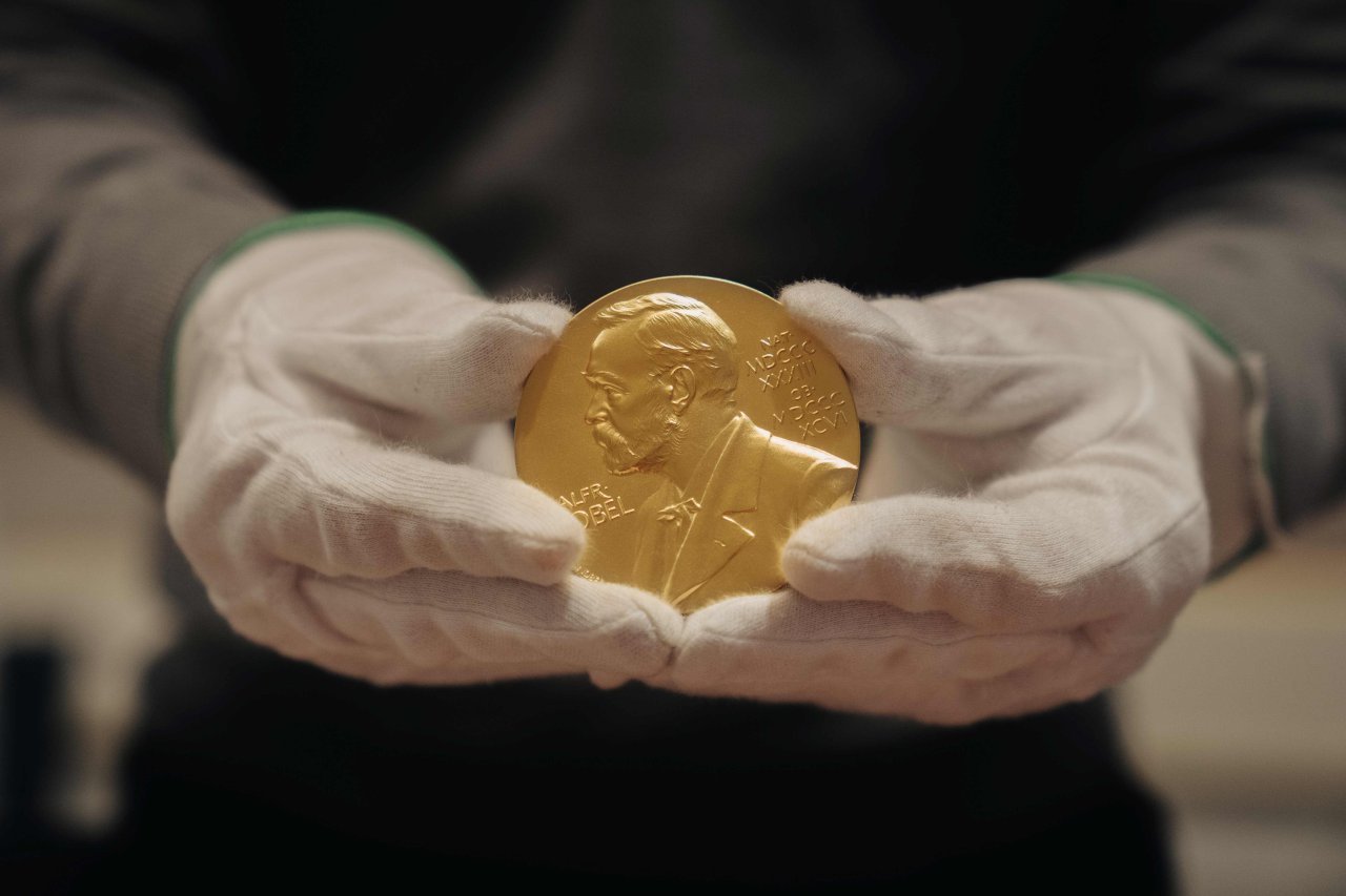 Jemand hält in beiden Händen, die in weißen Baumwollhandschuhen stecken, eine goldene Nobel-Preis-Münze/Medaille.