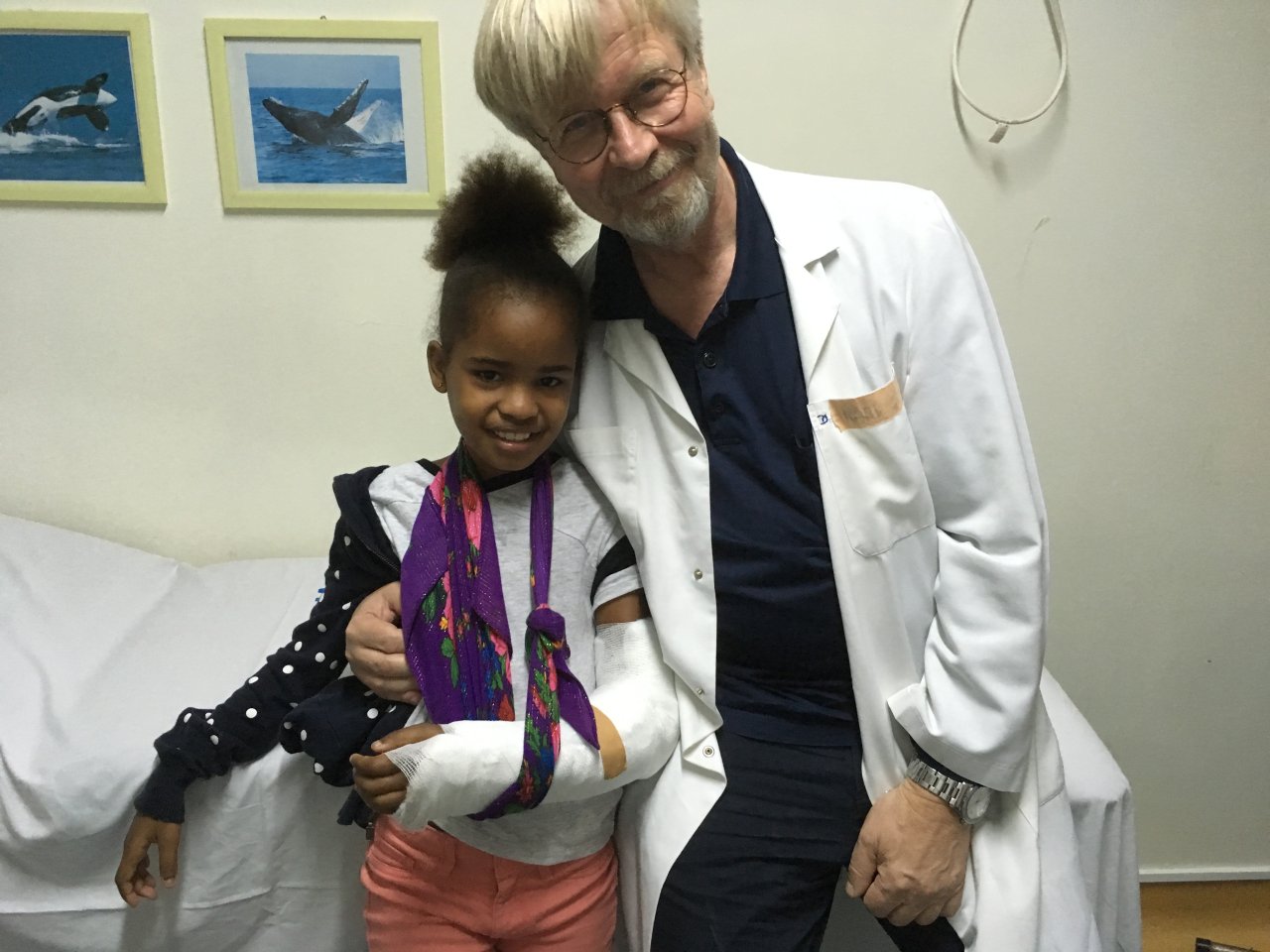 Ein Arzt sitzt neben einer jungen Patientin, die gerade einen Gips am linken Arm bekommen hat.