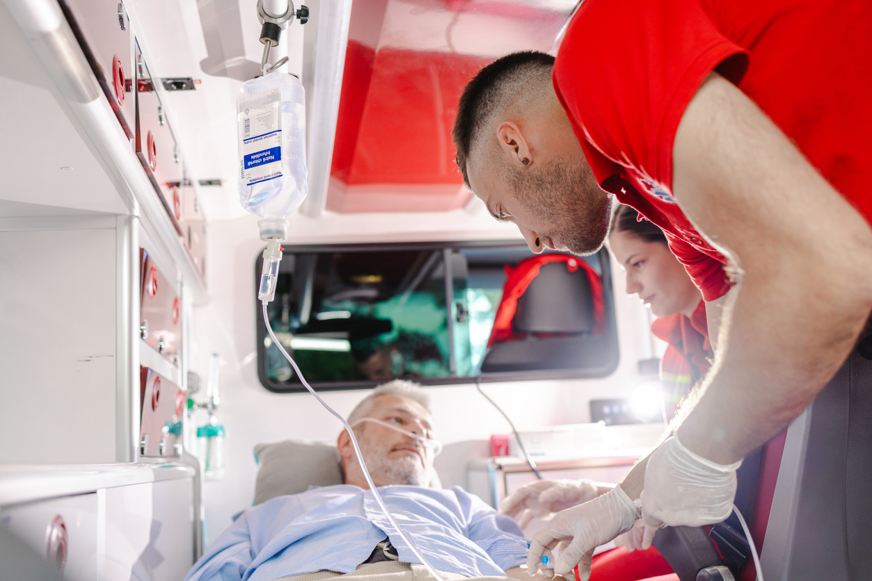 Ein Mann liegt in einem Rettungswagen und wird gerade von zwei Sanitäter*innen versorgt.