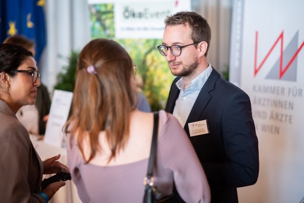 Drei Personen, ein Mann, der rechts steht und gerade in einem Gespräch mit zwei Frauen ist.