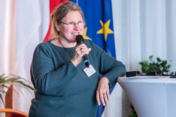 Eine Frau mit Mikrophon lehnt sich an einen Hochtisch an.