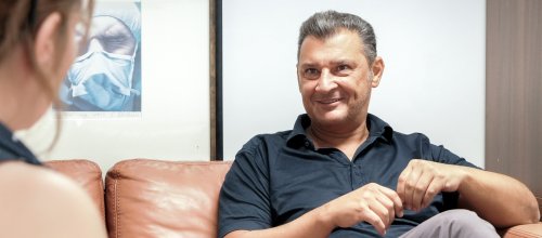Mann mit kurzärmligem Hemd sitzt im Gespräch auf einem Sofa. 