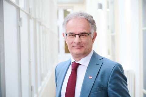 Mann im Sakko mit grauen Haaren und Brille. 
