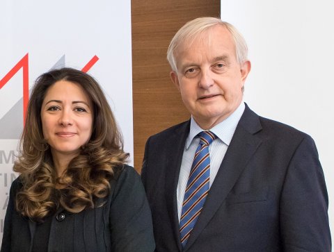 Zwei Personen, eine Frau, die links steht, und ein Mann, der rechts steht, blicken freundlich und direkt in die Kamera.
