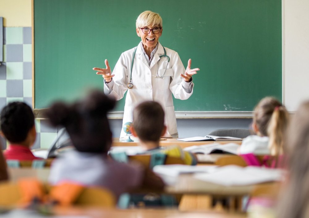 Eine Ärztin steht im Klassenzimmer und unterrichtet Gesundheit.
