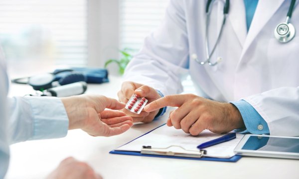 Man sieht auf dem Bild die Hände eines Arztes, der gerade Medikamente an einen Patienten übergiibt.