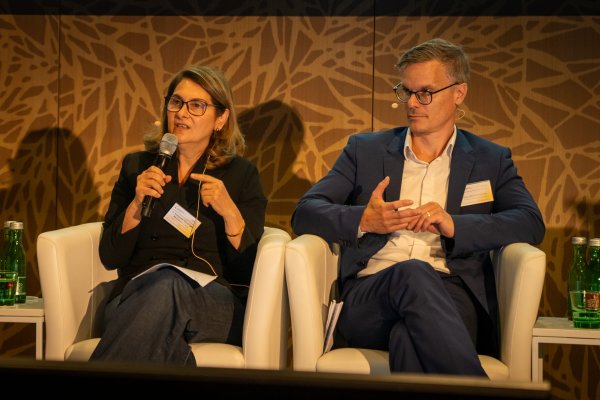 Eine Frau und ein Mann sitzen auf einem Podium einer Diskussionsrunde.