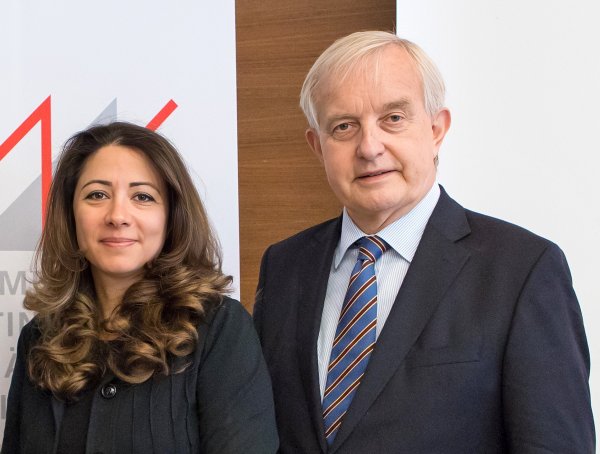Zwei Personen, eine Frau, die links steht, und ein Mann, der rechts steht, blicken freundlich und direkt in die Kamera.
